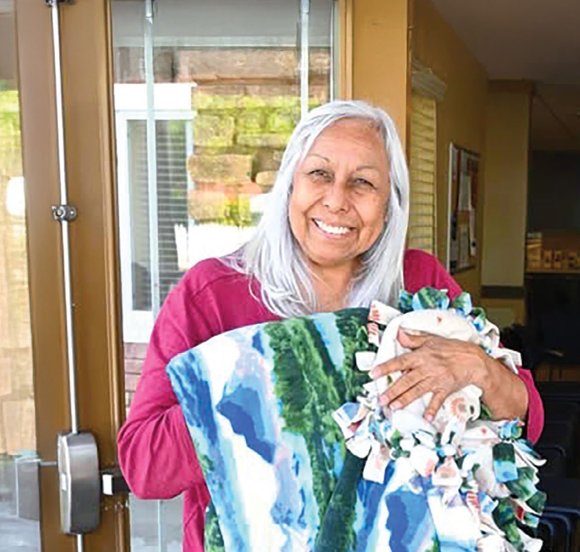 A smiling older woman holding a quilt in a report cover photograph